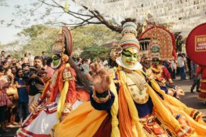 Colorfully dressed performers dance joyfully in a vibrant cultural parade, surrounded by an engaged crowd enjoying the festivities.