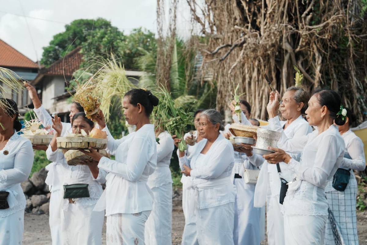 A group of women in traditional white attire participate in a ceremonial offering, holding baskets filled with ceremonial items.