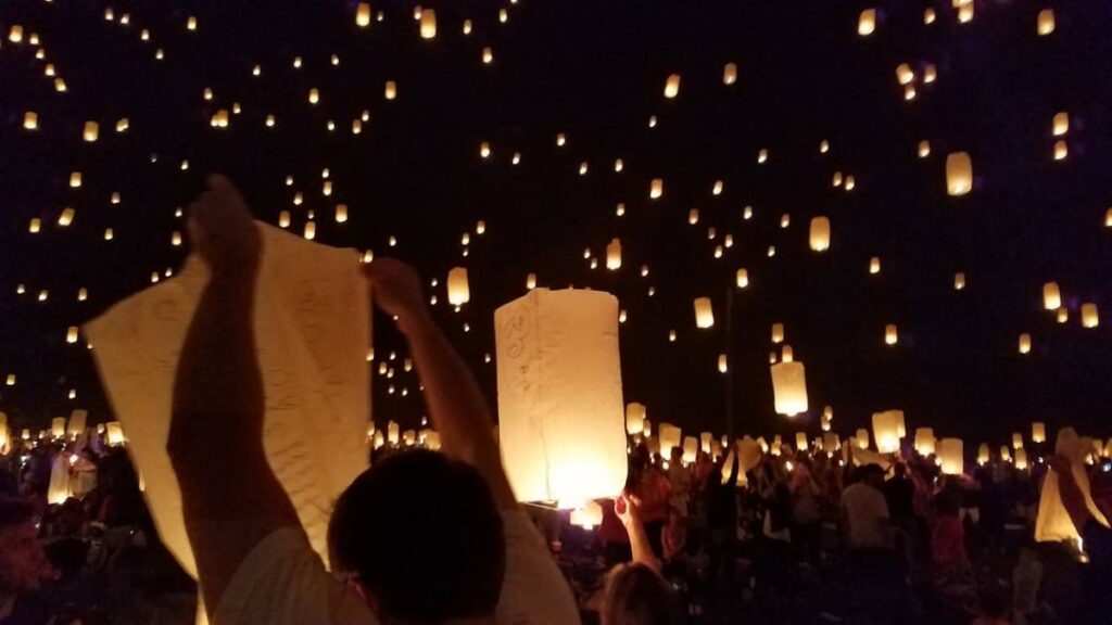 A crowd of people releases glowing lanterns into a dark sky, creating a magical atmosphere filled with floating lights.