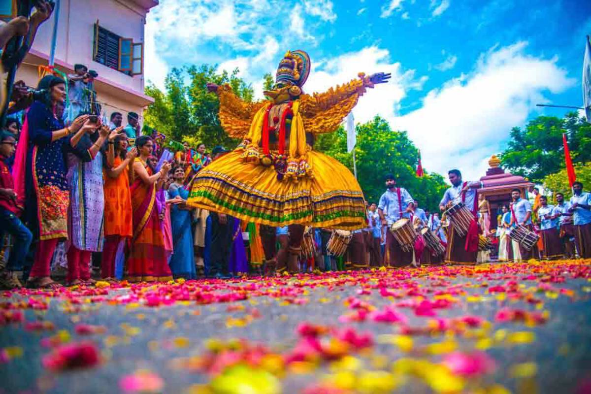 A vibrant cultural festival scene featuring a performer in a yellow costume dancing amidst a crowd, surrounded by flower petals.