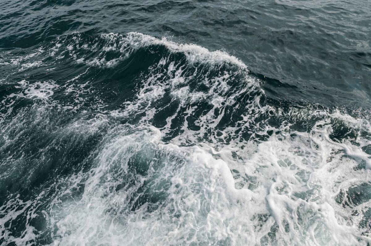 Waves rolling in dark turquoise water, creating white foam and ripples, evoking a sense of movement and tranquility on the ocean surface.