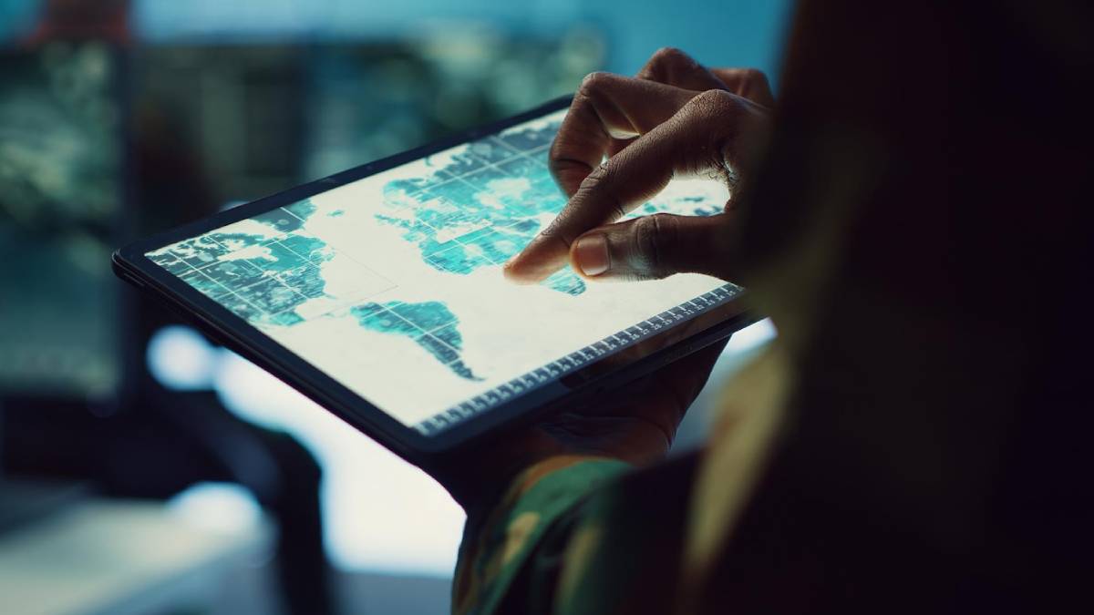 A close-up of a person using a tablet displaying a digital world map, highlighting global locations with a focus on technology in operation.