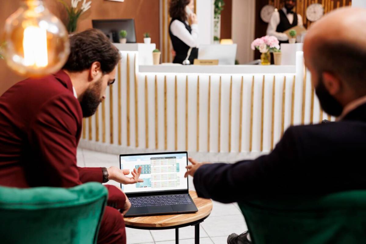 Two business professionals discuss over a laptop, showcasing a colorful data display, in a modern hotel lobby with a welcoming atmosphere.