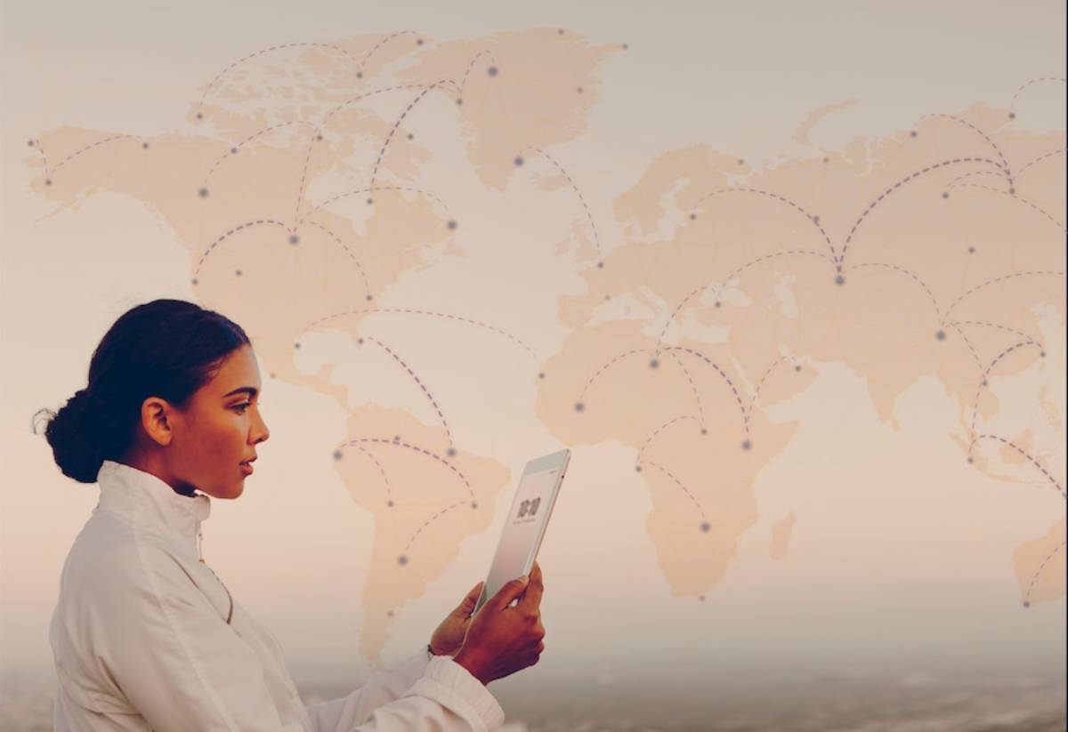 A person in a white jacket holds a tablet, overlooking a world map with network connections marked across continents.
