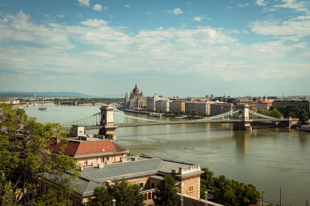 View of the Danube River with the iconic Chain Bridge and Hungarian Parliament Building against a cloudy sky in Budapest.
