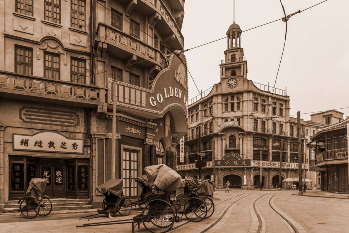 Vintage streetscape featuring classic architecture, rickshaws, and signs in an old city setting, rendered in sepia tones.