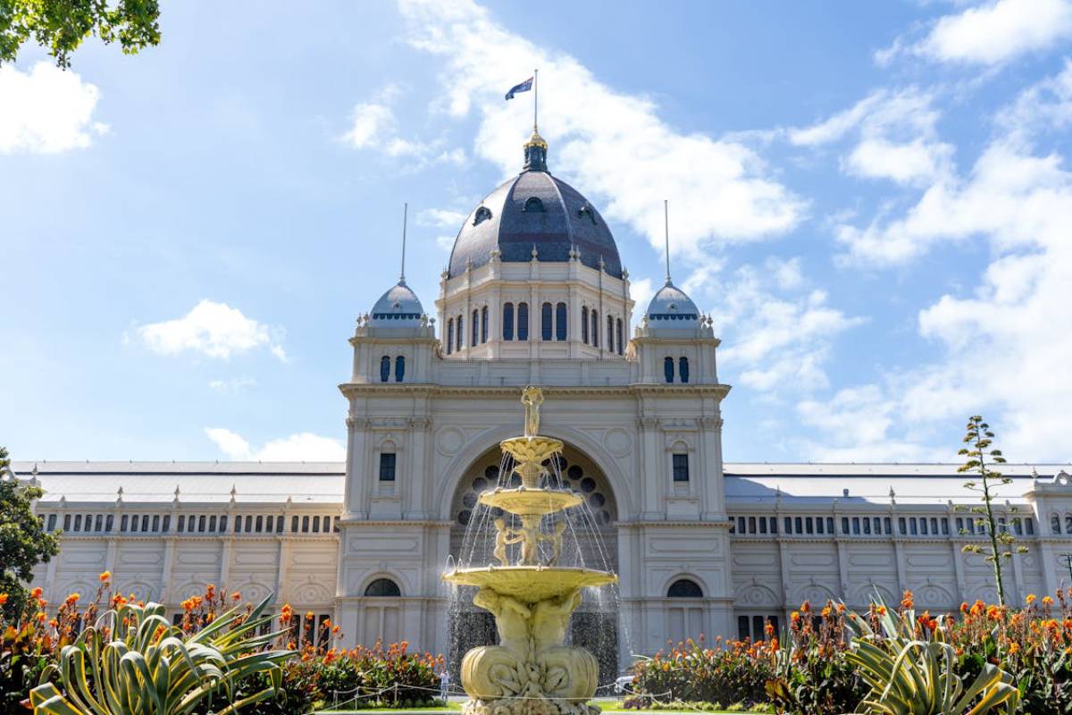 Royal Exhibition Building in Melbourne, featuring a grand fountain and vibrant flowers against a clear blue sky.