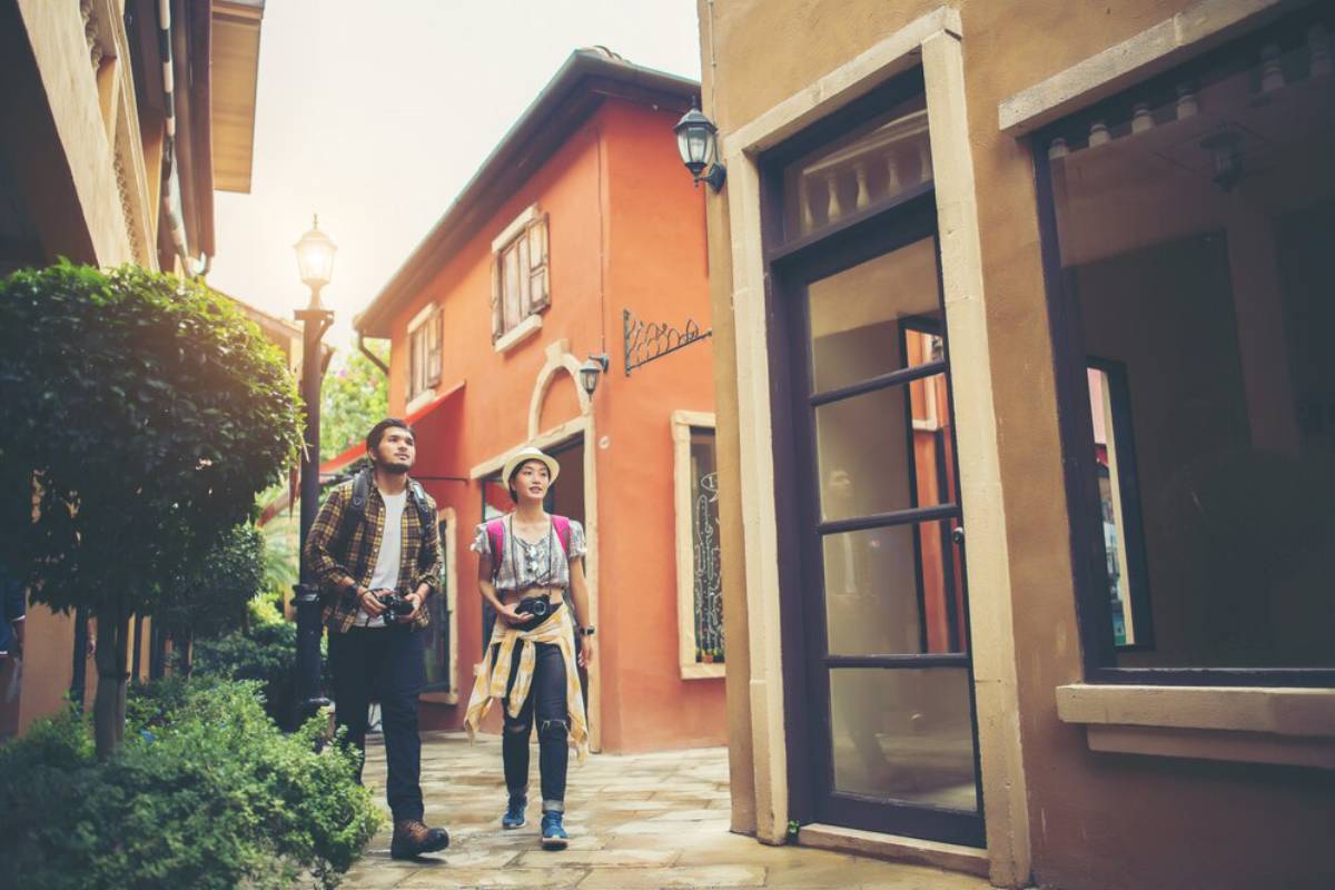 A couple strolls hand in hand through a charming cobblestone alley lined with colorful buildings and greenery.