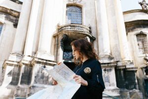 A person stands in front of an ornate, historic building, examining a map outdoors under clear blue skies.