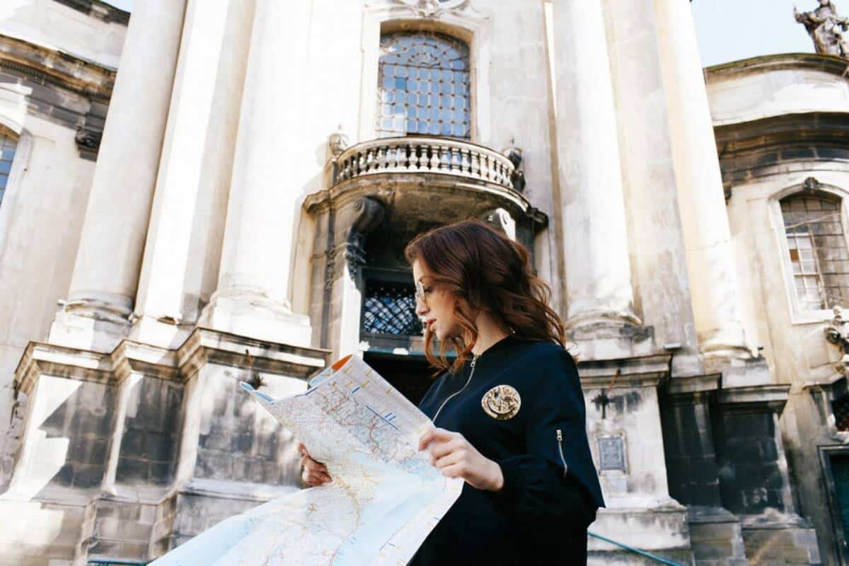 A person stands in front of an ornate, historic building, examining a map outdoors under clear blue skies.