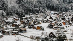 A picturesque snowy village nestled among tall trees, featuring traditional wooden houses and a serene, wintry landscape.