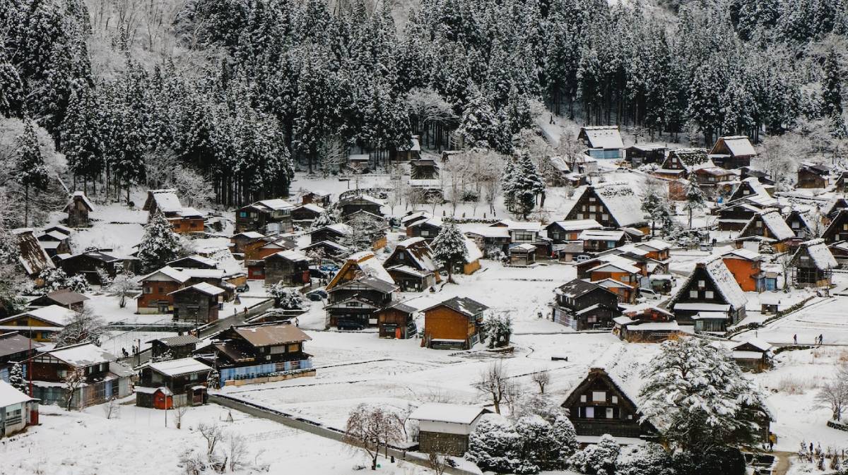 A picturesque snowy village nestled among tall trees, featuring traditional wooden houses and a serene, wintry landscape.