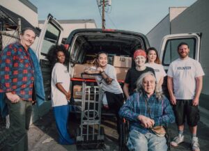 A group of volunteers poses in front of a van filled with aid boxes, showcasing their commitment to community support.