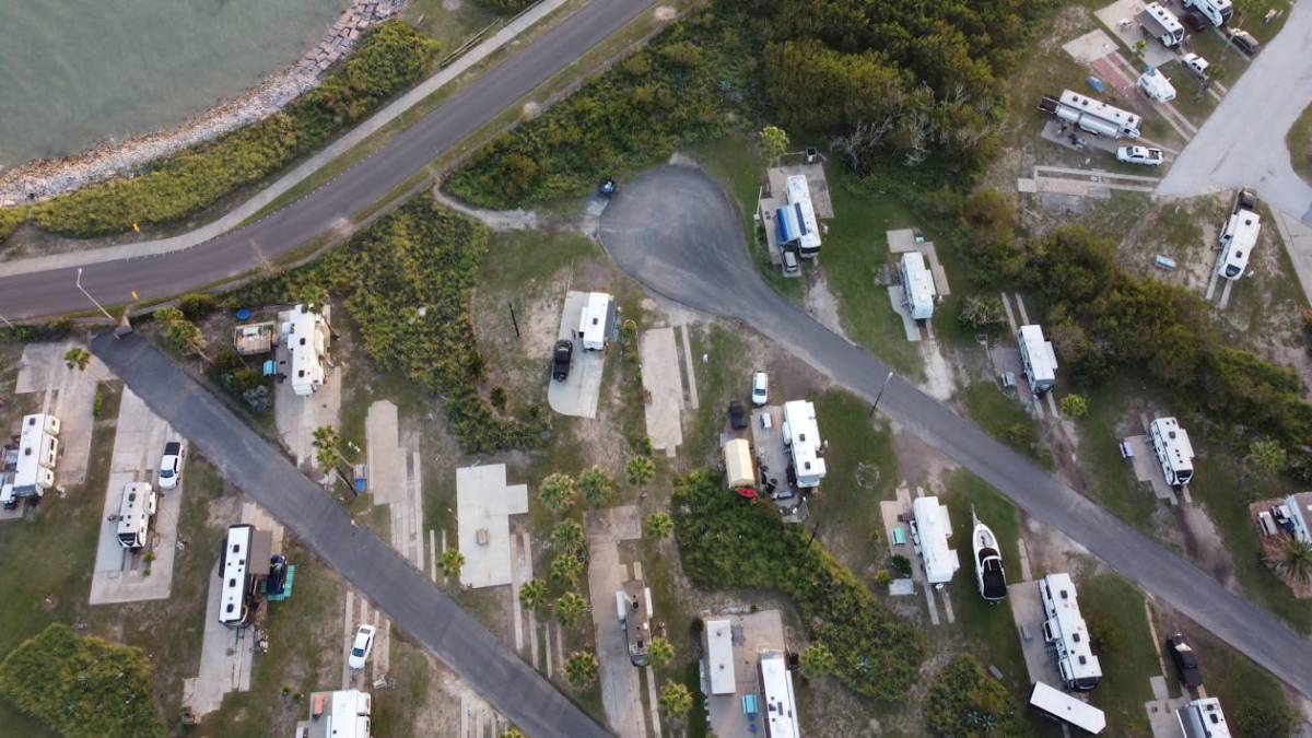 Aerial view of an RV park by the coast, showcasing numerous RVs parked along winding roads and grassy areas.