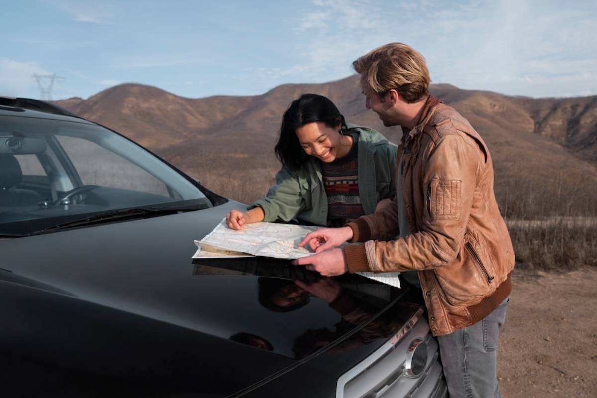 Two people study a map on the hood of a black car, with mountains in the background under a clear sky.