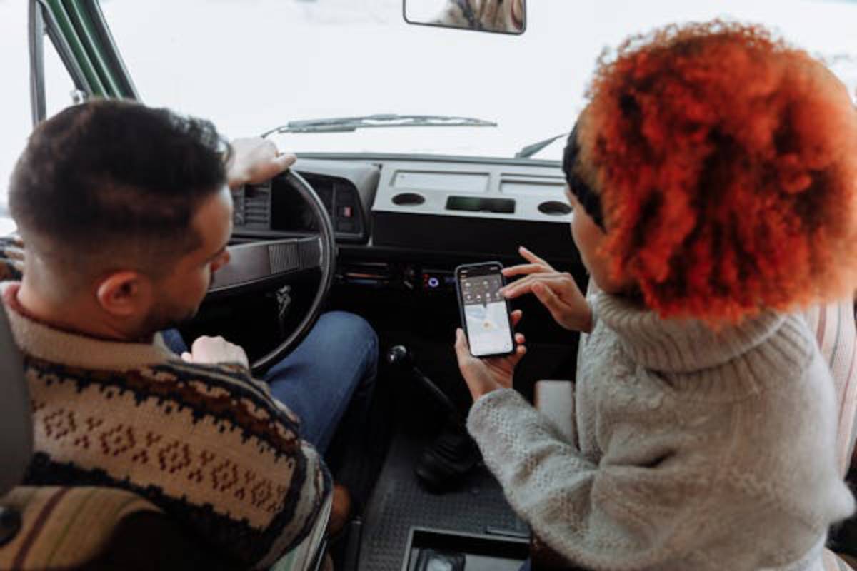 A person in a cozy sweater shows something on their phone to the driver in a vintage van, with a snowy backdrop visible outside.